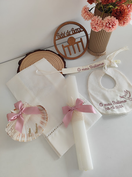 Conjunto para batismo com toalha, vela, concha, babete bordada, marcador e vaso com flores.