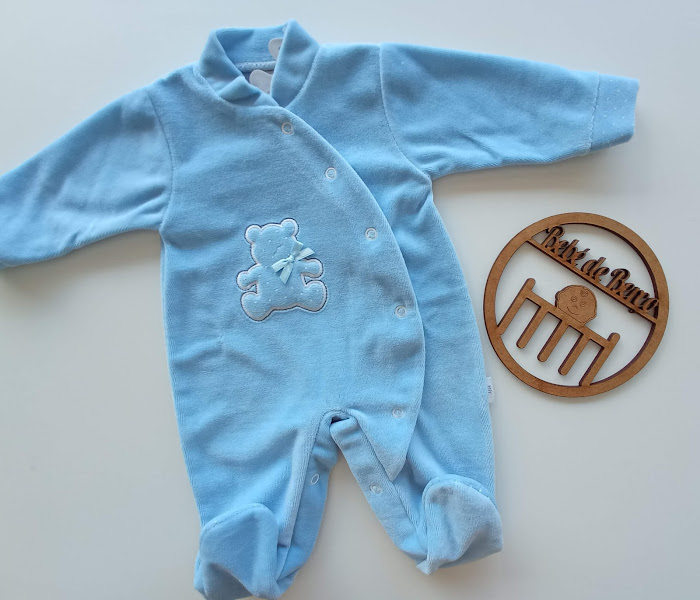 Macacão azul para bebé com ursinho bordado e fecho de botões ao lado de placa de madeira