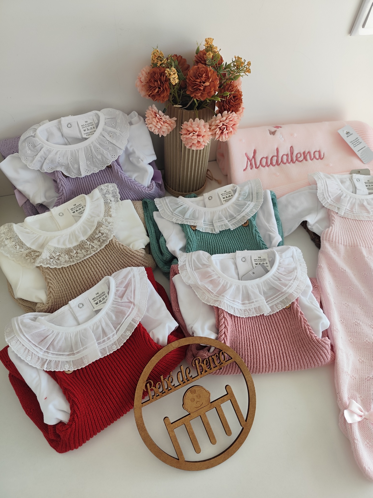 Conjunto de roupa de bebé com vestidos de malha coloridos, cobertor rosa bordado e flores em vaso