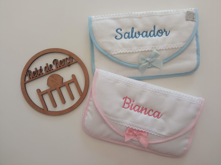 Duas bolsas bordadas com nomes em azul e rosa e suporte de madeira redondo com texto