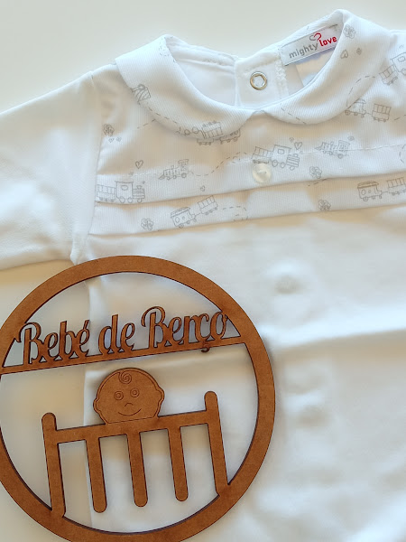 Macacão branco para bebé com padrão de comboios cinza e decoração em madeira com texto 'Bebé de Berço'.