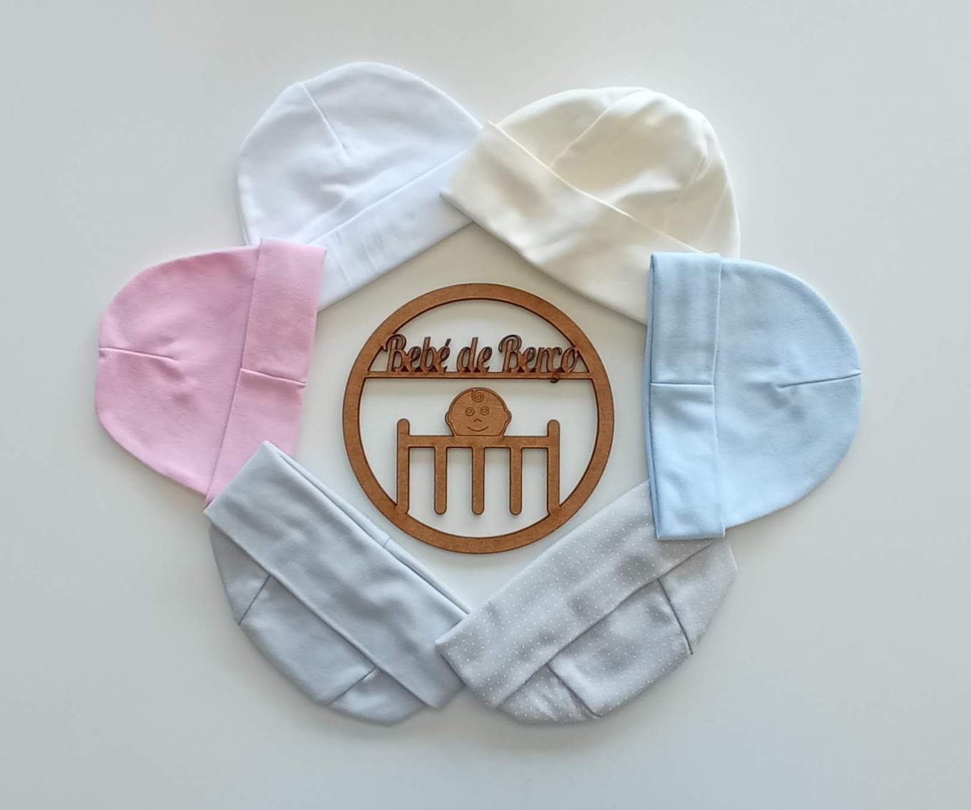 Cinco gorros de bebé em várias cores dispostos em círculo com uma placa de madeira 'Bébé de Reros' ao centro