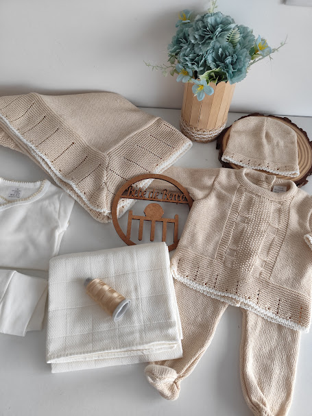 Roupas de bebé em malha bege com detalhes brancos e acessórios em fundo branco