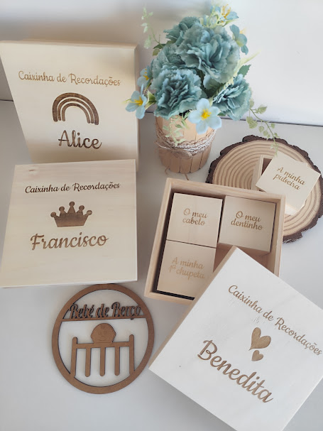 Caixinhas de recordações personalizadas em madeira com nomes gravados e pequenos blocos para guardar memórias, decoradas com flores artificiais azuis e brancas.