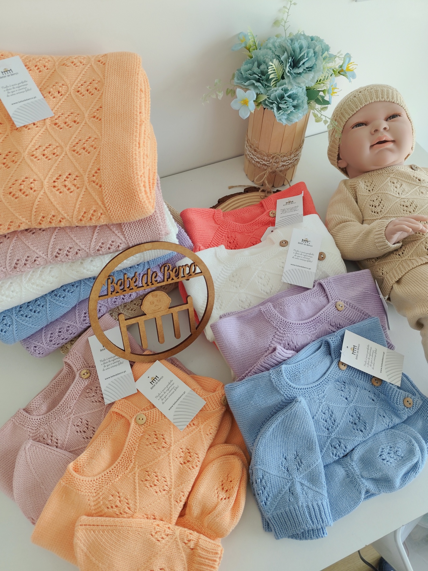 Roupas de malha coloridas para bebés, manequim vestido e flores num vaso