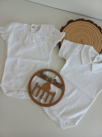 Dois bodies de bebé brancos com diferentes golas e botões de pressão, sobre superfície branca com decoração em madeira