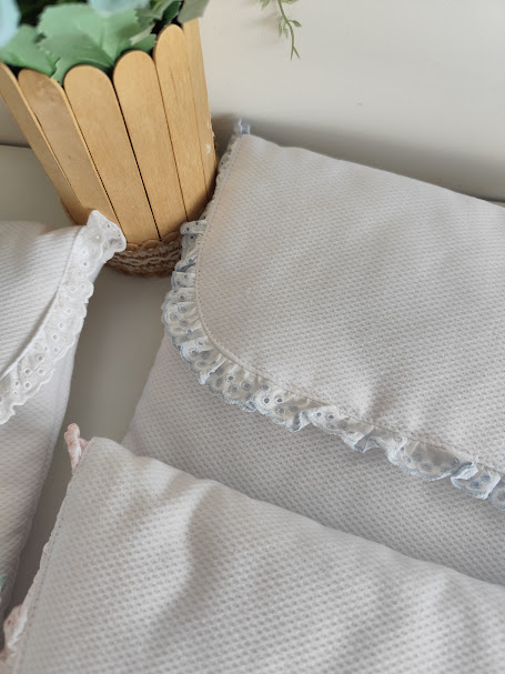 Almofadas brancas com detalhes em renda e vaso decorativo de madeira com planta artificial