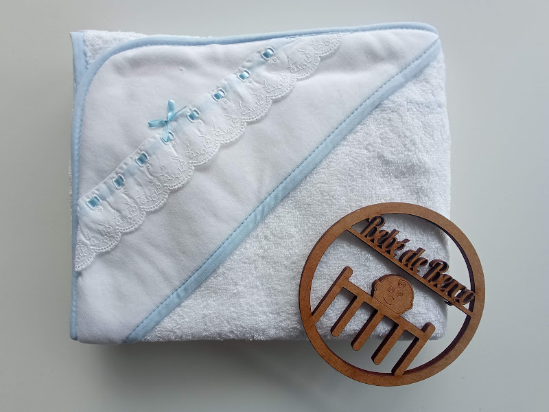 Toalha de bebé branca com bordado azul e objeto redondo de madeira
