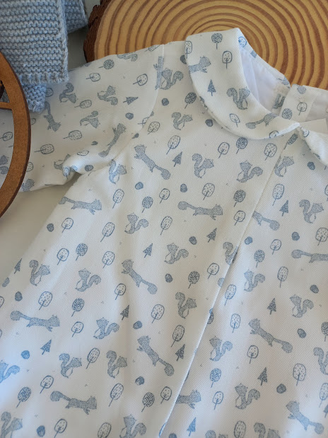 Peça de roupa de bebé branca com padrões azuis de animais e árvores.