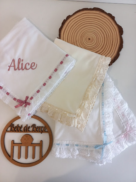 Três paninhos brancos com rendas coloridas e nome bordado Alice sobre mesa branca com suporte de madeira e adereço de madeira