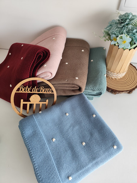 Mantas em malha coloridas com pompons brancos e decoração com flores em vaso e placa de madeira