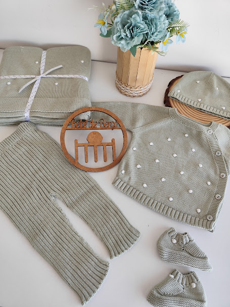 Conjunto de roupa de bebé tricotada em verde-acinzentado com pontos brancos sobre uma superfície branca