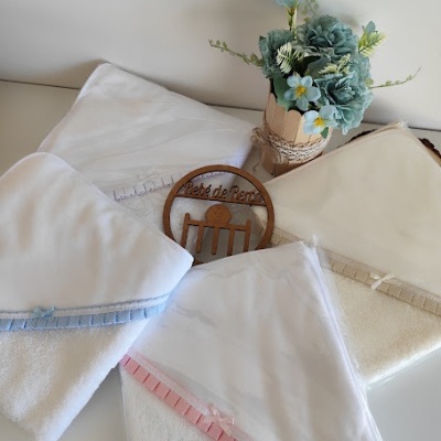 Toalhas brancas com bordado azul e rosa, placa de madeira redonda e vaso com flores azuis e verdes