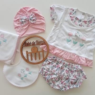 Conjunto de roupa para bebé com flores, touca rosa, babete e toalha bordados, sobre superfície branca