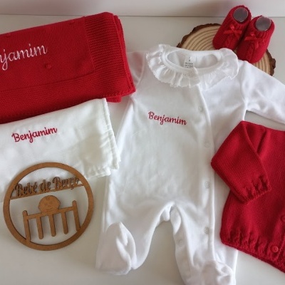 Conjunto de roupa de bebé com manta, macacão, casaco e botas vermelhas e brancas, nomes bordados e suporte de madeira com texto
