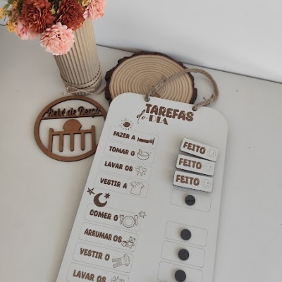 Quadro branco de tarefas diárias com texto em português, ícones e legendas móveis, jarro com flores coloridas ao lado, superfície branca.