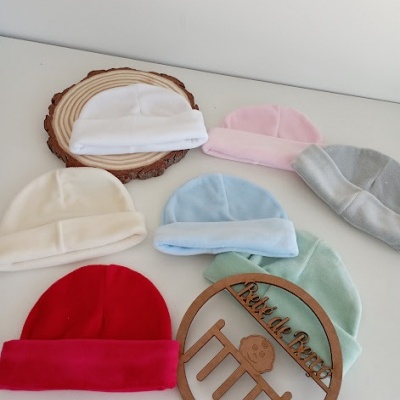 Seis gorros de bebé de várias cores sobre superfície branca com suporte redondo de madeira e círculo de madeira decorativo