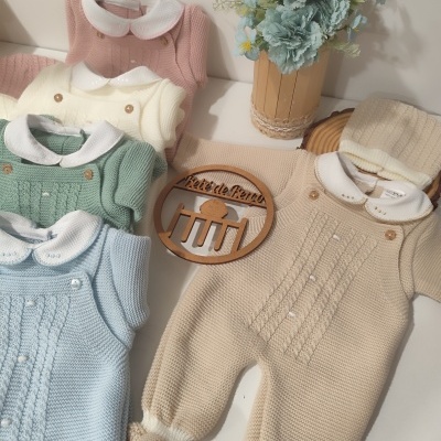 Conjunto de roupa de bebé em malha de várias cores dispostas com vaso de flores ao lado.