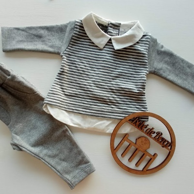 Conjunto de roupa para bebé com camisola às riscas e calças cinzentas junto a objeto decorativo redondo em madeira