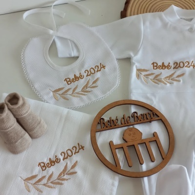 Conjunto de roupa de bebé branco com bordados castanhos e ornamento de madeira