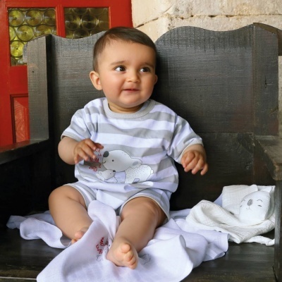 Bebé numa cadeira de madeira vestindo t-shirt às riscas cinzentas com elefante e calções brancos, com toalha branca ao lado