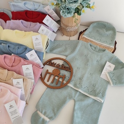 Conjunto de roupa de bebé azul esverdeado com padrão e gorro em mesa com flores e mais conjuntos coloridos