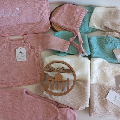 Roupa de bebé em malha colorida disposta numa caixa com etiquetas e manta bordada