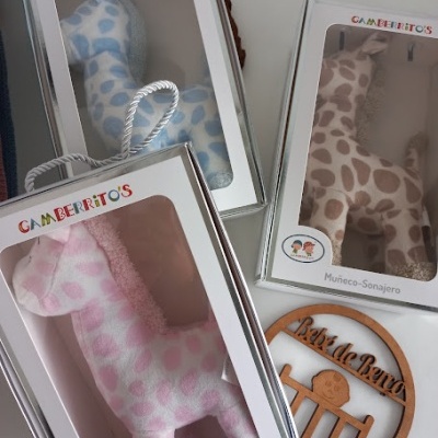 Brinquedos sonâjeros em embalagem branca e um ornamento de madeira sobre mesa branca.