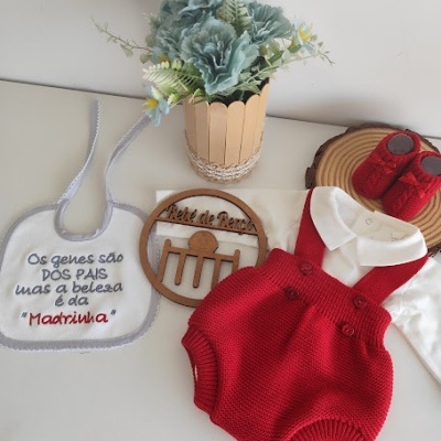 Conjunto de roupa de bebé com babete, jardineira vermelha, body branco, sapatinhos vermelhos e vaso com flores azuis