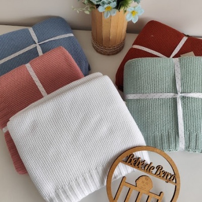 Conjunto de mantas coloridas em tecido de malha com fita branca e decoração com plantas e ornamento de madeira