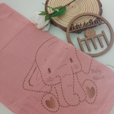 Toalha rosa para bebé com padrão de elefante e objeto decorativo de madeira.