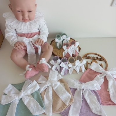 Boneca de bebé com roupa branca e rosa e roupas de malha coloridas com fitas grandes brancas