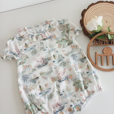 Conjunto de bebé branco com padrão de animais e bicicletas, gola com folho e botões na zona da fralda.