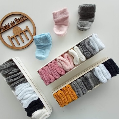 Caixas abertas com meias de bebé coloridas e uma placa de madeira redonda com texto