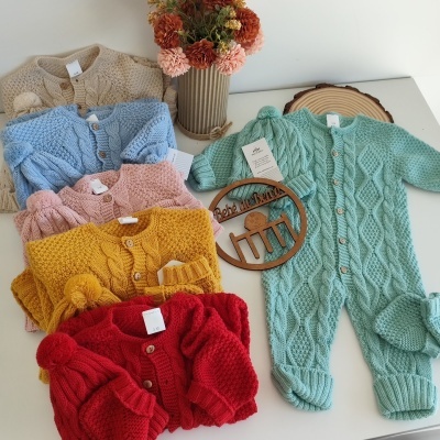 Roupas de bebê em malha tricotada de várias cores sobre fundo branco com vaso de flores e placa de madeira