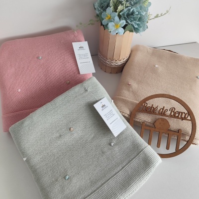 Três mantas de malha com pompons coloridos e decoração de flores e placa de madeira