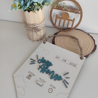 Placa decorativa com informações de nascimento, vaso com flores artificiais e enfeite de madeira em mesa