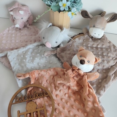 Quatro paninhos de pelúcia com cabeça de animal e textura de bolinhas junto a vaso com flores azuis