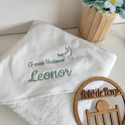 Toalha de bebé branca bordada a verde com texto, vaso de flores artificiais e decoração de madeira circular