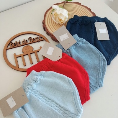 Peças de roupa de malha de bebé em várias cores com etiquetas e placa decorativa 'Bebé de Renas' numa mesa.