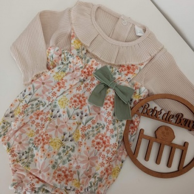 Body de bebé floral com mangas longas bege e laço verde ao lado de moldura de madeira