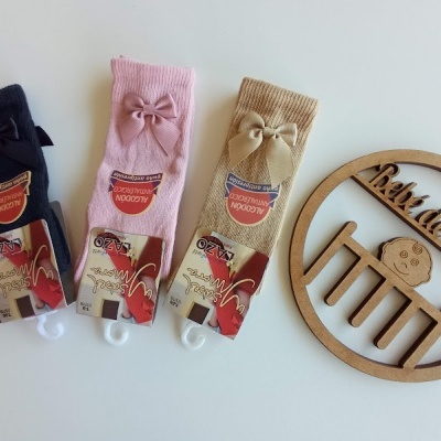 Três pares de meias de bebé azul escuro, rosa e bege com laço e etiquetas, e enfeite de madeira 'Bebe a Bordo'