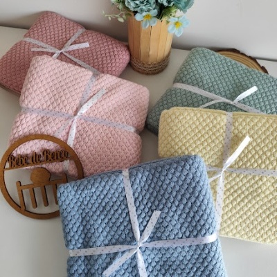 Mantinhas de bebê texturizadas em várias cores com fita branca, vaso de flores e placa de madeira