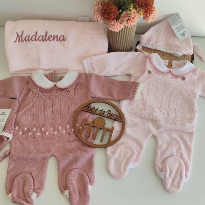 Macacões de bebé rosa e rosa claro, manta bordada, gorro, placa de madeira e flores secas