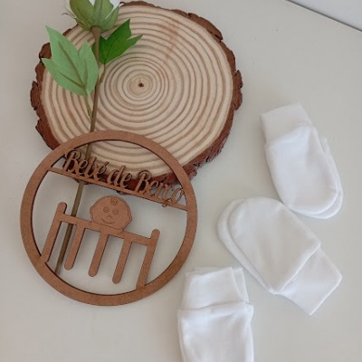 Luvas brancas para bebé e decoração de madeira com frase 'Bela de Berço' sobre disco de madeira