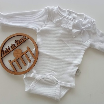 Body de bebé branco com manga comprida e laço ao lado de anel de madeira com texto