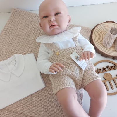 Boneco bebé vestido com roupa branca e bege, manta e decoração em madeira