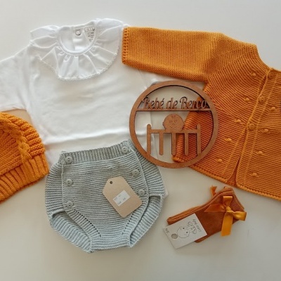 Conjunto de roupa de bebé com camisola branca, casaco e touca laranja, cuecas cinzas e sapatos laranja