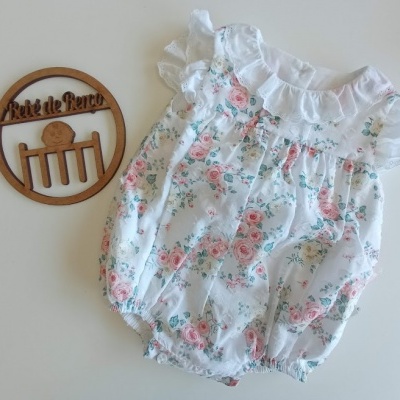 Body de bebé branco com padrão floral e folhos ao lado de placa decorativa de madeira