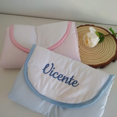 Duas toalhas para bebé, rosa e azul, com nome bordado 'Vicente' numa superfície branca com decoração de madeira e flor